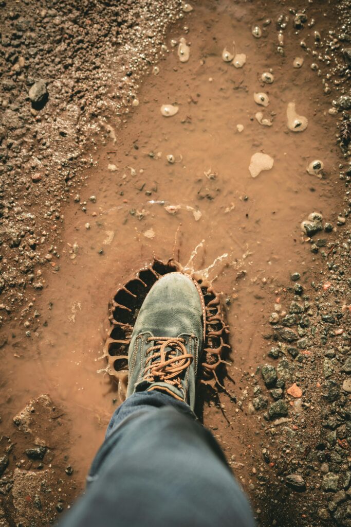 pexels-photo-1914815-1914815 A single boot stepping into a muddy puddle outdoors, creating a splash on a dirt road.